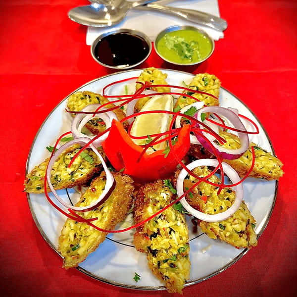 Indian appetizer platter with fried fritters, red onions, lemon, and two dipping sauces on a red tablecloth.