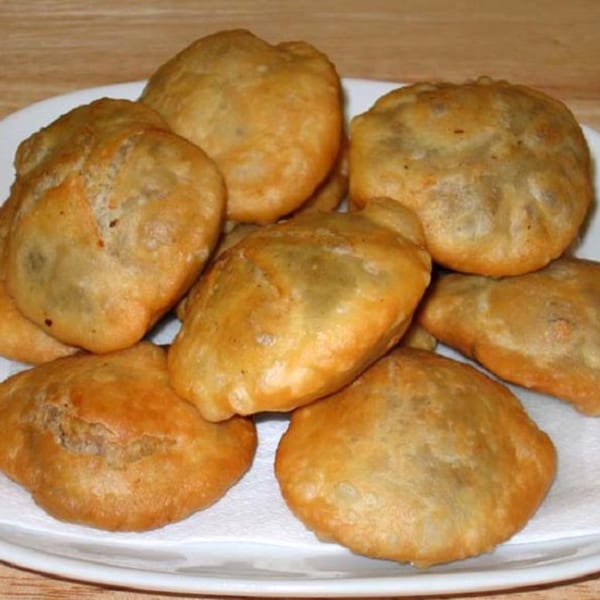 A plate of golden-brown, fried Indian puri bread, some resting on a white paper towel.
