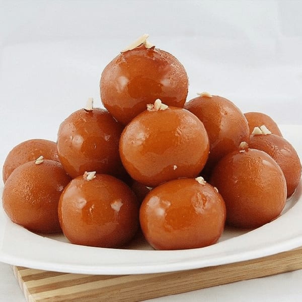 A white plate piled high with glistening, brown gulab jamun, garnished with slivered almonds.