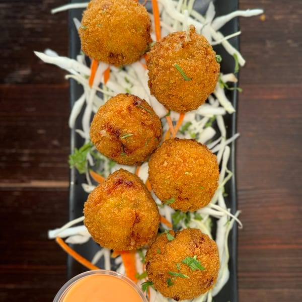 Six golden-brown Indian croquettes, garnished with herbs, on a bed of shredded cabbage and carrots.