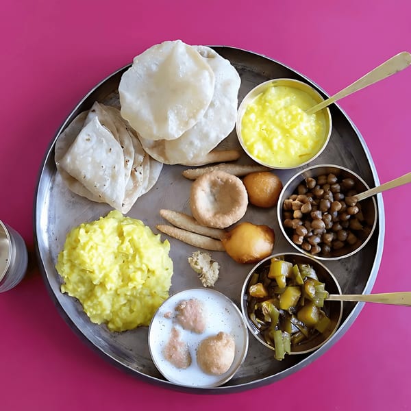 A Kesar's Indian Thali with various dishes, including flatbreads, curries, and desserts, on a pink background.