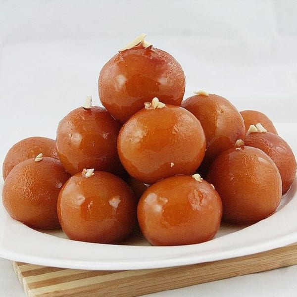 A white plate piled high with glistening, brown gulab jamun, garnished with slivered almonds.