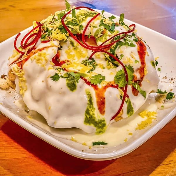 Indian chaat, a savory snack, topped with white yogurt, green chutney, red sauce, and crispy sev.