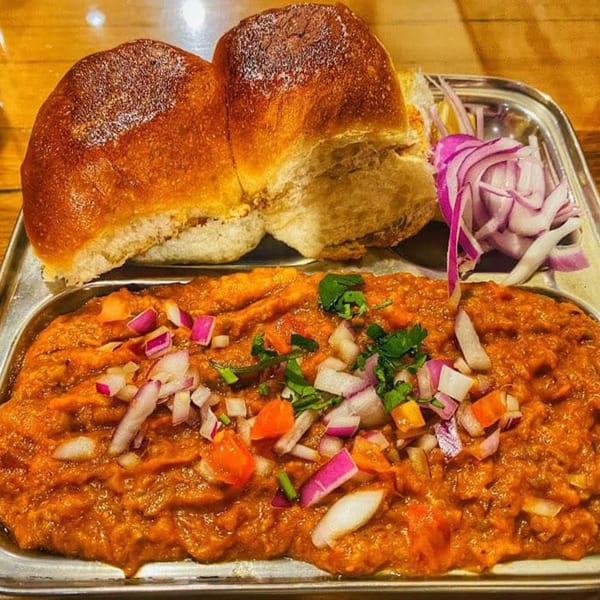 Kesar's Indian Thali pav bhaji, a vibrant orange vegetable curry with chopped onions, cilantro, and bread.