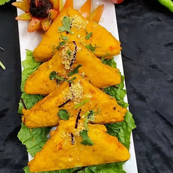 Four golden Indian samosas, garnished with cilantro and sev, on a bed of lettuce.