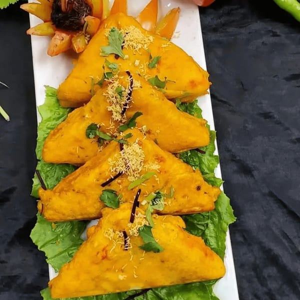 Four golden-brown Indian bread pakoras, garnished with cilantro and sev, on a bed of lettuce.